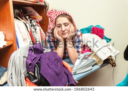 Portrait of tired housewife in pile of not ironed clothes