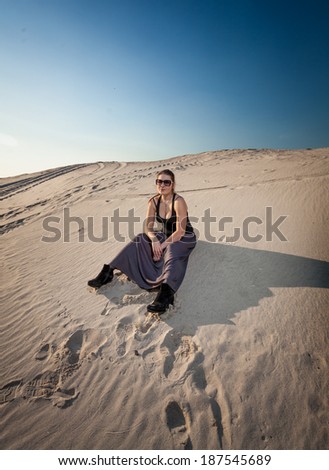 Beautiful woman in dress sitting on sand dune