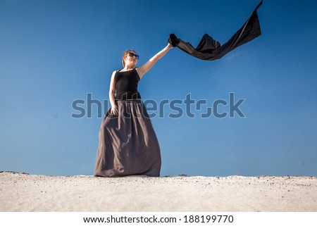 Beautiful woman in long dress with black cloth standing on sand dune