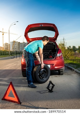 Photo of man changing punctured wheel on broken car