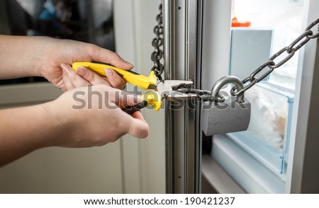 Conceptual photo of woman trying to cut chain on fridge with pliers