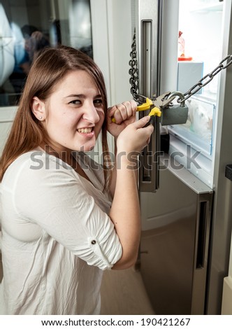 Portrait of angry woman cutting chain on refrigerator with cutters