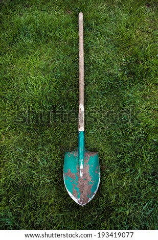 Photo of metal green shovel with wooden handle on grass lawn