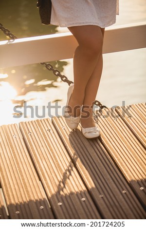 Beautiful slim legs in ballet flats on wooden bridge at summer day
