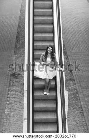 Black and white photo of woman with shopping bag descending the escalator