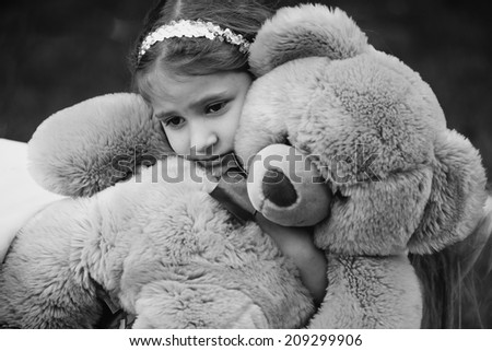 Black and white portrait of small crying girl hugging teddy bear
