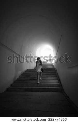 Monochrome shot woman going up the stairs at tunnel with light in the end