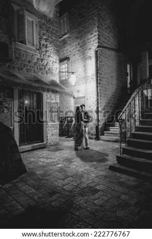 Black and white shot of beautiful romantic couple kissing at night on street of old city