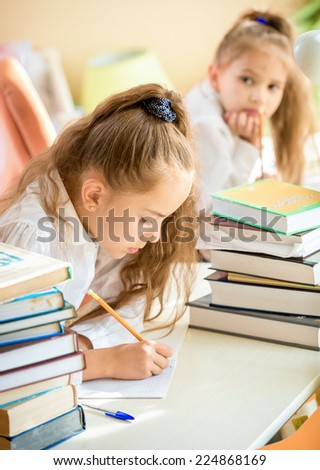Portrait of concentrated girl doing homework while classmate trying to write off