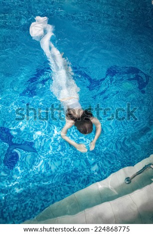Sexy woman in long white dress diving underwater at swimming pool