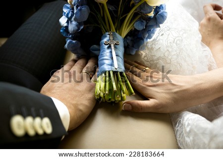 Closeup shot of bride and groom holding hands on wedding bouquet at car