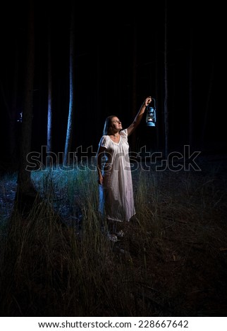 Brunette woman with gas lantern lighting up forest at night