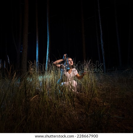 Young woman in nightgown sitting in high forest at night with lantern