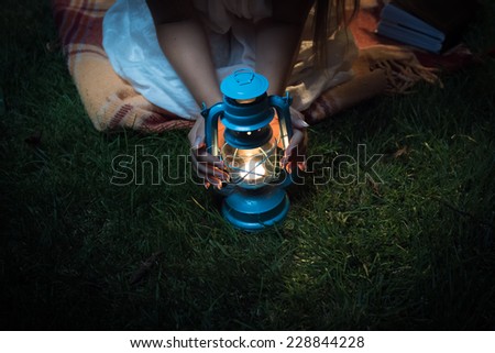 Closeup shot of woman sitting on grass at night and holding hands on lantern