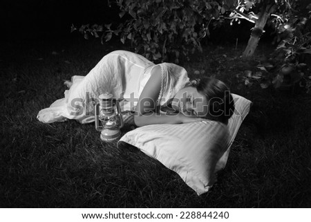 Black and white photo of woman sleeping at garden at night