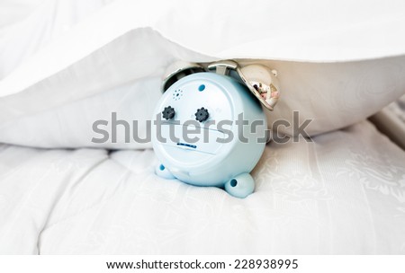 Closeup conceptual photo of alarm clock under pillow on bed