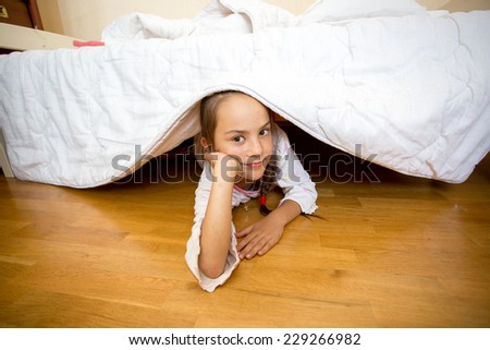 Portrait of little girl lying on floor under bed