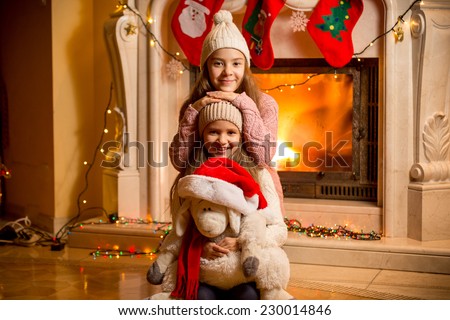 Closeup portrait of two beautiful girls in sweaters sitting at fireplace at house