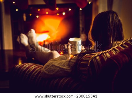 Toned photo of woman warming up with hot tea at fireplace at winter