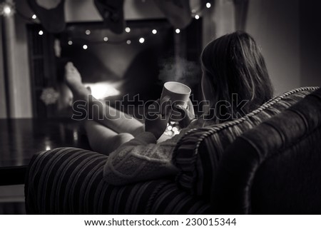 Black and white photo of cute woman sitting at fireplace with cup of tea
