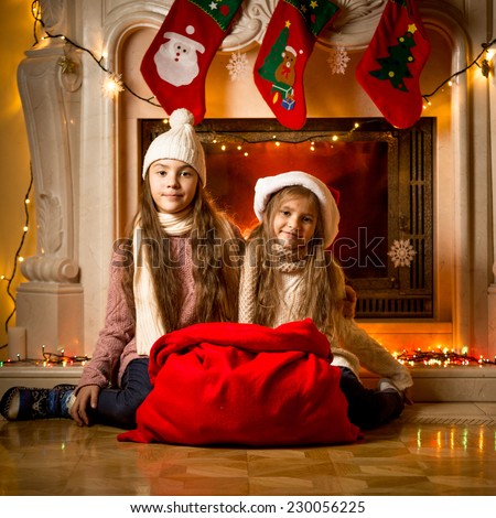 Beautiful girls sitting next to fireplace with big red bag for gifts