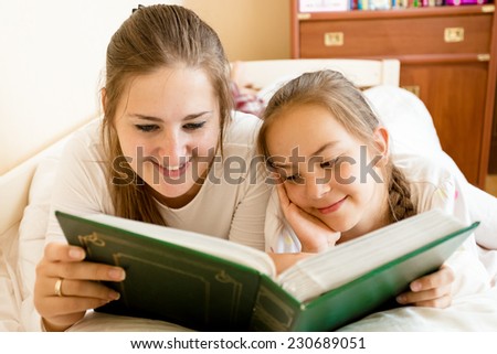 Portrait of smiling mother and daughter reading big book at bed