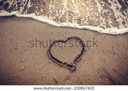 Closeup toned photo of heart drawn on sand sea beach