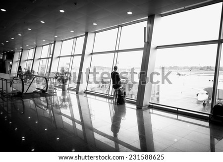 Black and white photo of woman standing in front of big panoramic window at airport