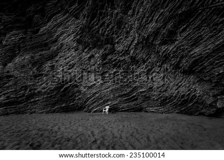 Black and white shot of white chair standing on deserted beach with high cliff