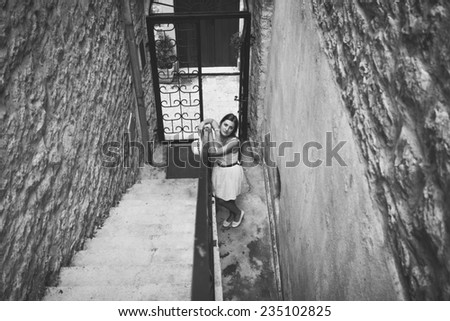 Black and white photo of young woman standing at entrance old building with stone stairs