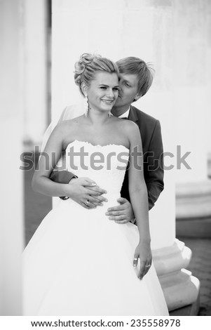 Black and white portrait of young groom hugging smiling bride from back