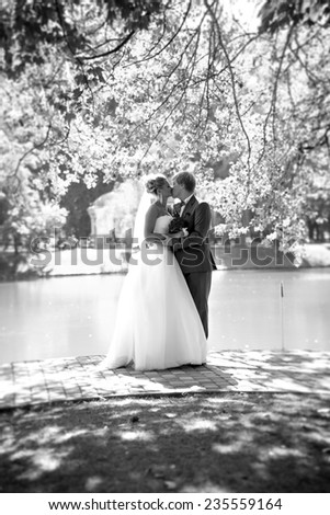 Black and white full length portrait of kissing bride and groom at park near the river