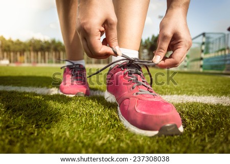 Closeup shot of woman tying laces on sneakers on grass field