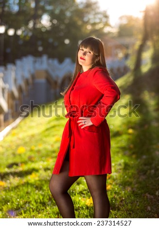 Portrait of beautiful brunette woman in red coat posing at autumn forest