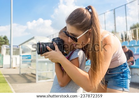 Portrait of young woman teaching little girl to photograph using professional camera