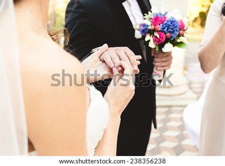 Closeup photo of beautiful young bride putting wedding ring on grooms finger