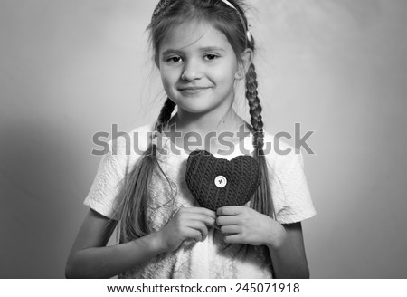 Monochrome portrait of cute smiling girl holding decorative heart on chest