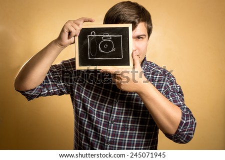 Portrait of handsome young man holding camera drawn on small blackboard