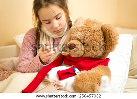 Portrait of little girl giving medicines to teddy bear