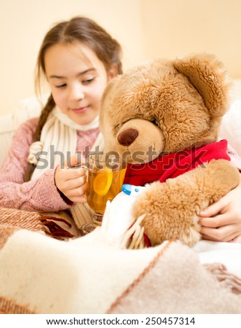 Closeup photo of sick girl lying in bed and giving tea to teddy bear