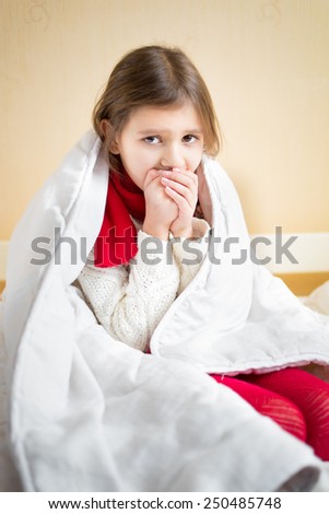 Portrait of sick little girl coughing on bed under blanket