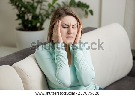 Young woman sitting on sofa and suffering from head ache