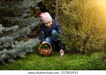 Beautiful smiling girl taking Easter egg form under the bush a backyard