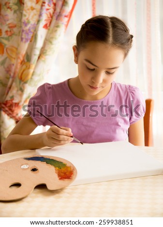 Portrait of concentrated girl drawing on canvas by oil paints