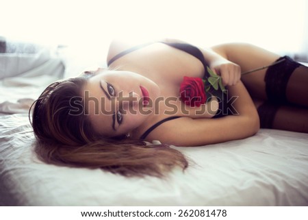 Toned portrait of sexy woman lying on bed with red rose
