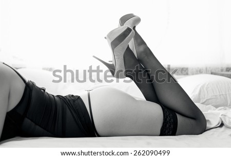 Black and white photo of sexy naked woman in stockings and high heels on bed