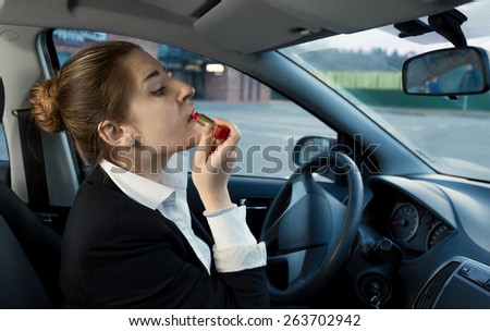 Beautiful businesswoman applying cosmetics while driving a car