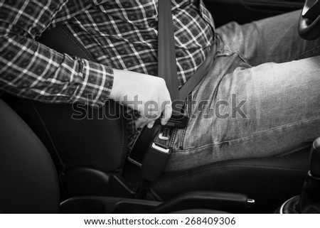 Black and white closeup photo of man fastening seat belt in car