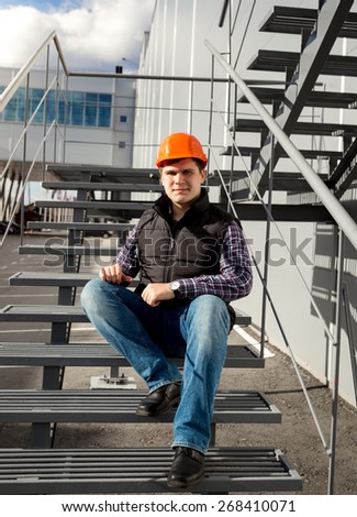 Handsome smiling worker relaxing on metal staircase during break