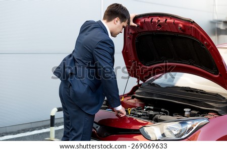 Young businessman in suit opening bonnet of open car